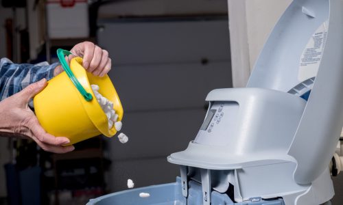 Salt crystals are added to a water softener via a bucket that is yellow